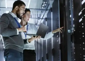 Male IT specialist holding a laptop discussing server support, virtual machines, and data centers with a female colleague. Managed IT Services